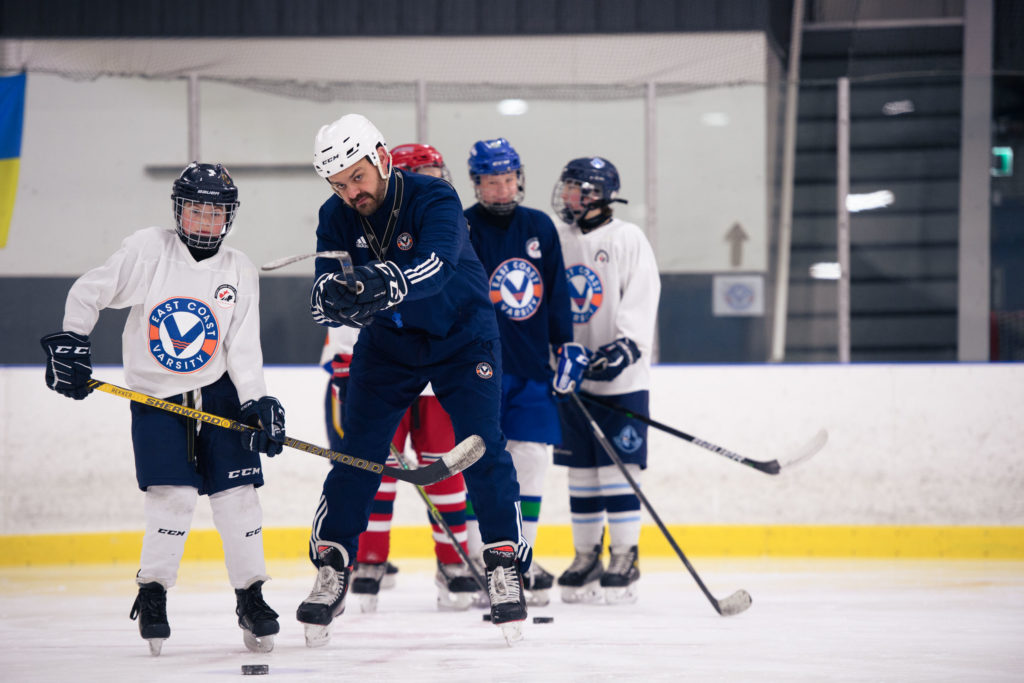 A teacher showing a student how to perform a hockey drill.