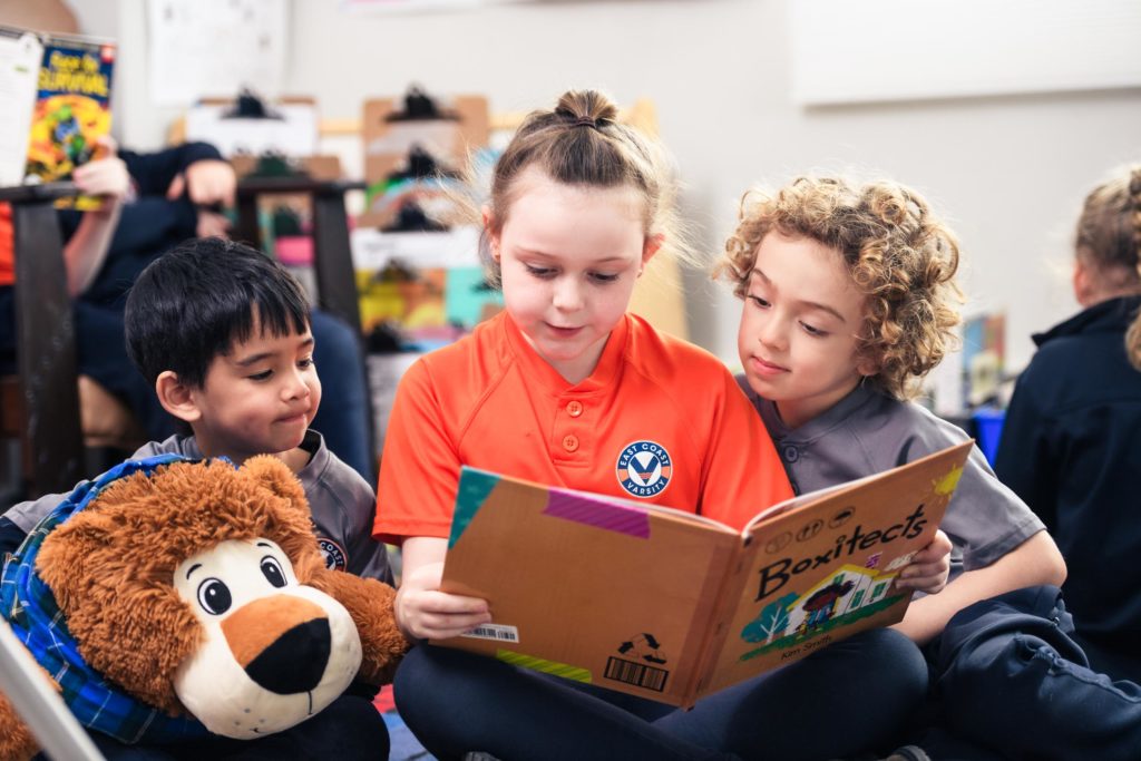 Three students reading together, one is holding a stuffed animal.